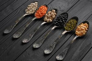 Variety of legumes in old silver spoons on a black wooden background. photo