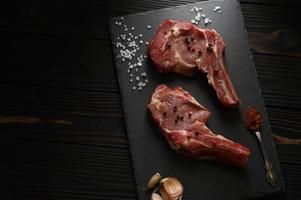 Raw cowboy steak and spices on a black wooden background. photo