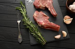 Raw cowboy steak and spices on a black wooden background. photo
