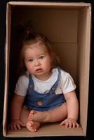 Happy little girl sitting in a cardboard box and having fun photo