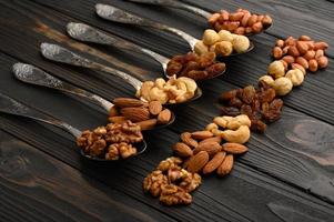 Hazelnut, cashews, raisins, almonds, peanuts, walnuts in silver spoons on a rustic background photo