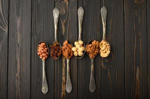 Hazelnut, cashews, raisins, almonds, peanuts, walnuts in silver spoons on a rustic background photo
