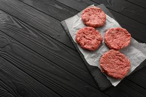 Raw beef burger patties on butcher's wooden board, rosemary and pepper. Black background. View from above. photo