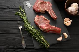 Raw cowboy steak and spices on a black wooden background. photo