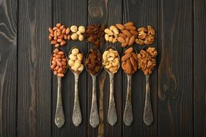 avellanas, anacardos, pasas, almendras, cacahuetes, nueces en cucharas de plata sobre un fondo rústico foto