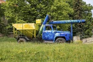 Old heavy truck machinery parked on grass against trees in historic town photo