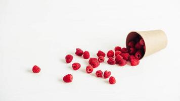 Fresh red raspberries in a paper cup on a white table background photo