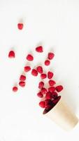 Fresh red raspberries in a paper cup on a white table background photo