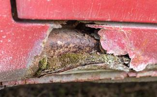 Rusty driver's door sills. Corrosion of the body of a red old car after winter. Influence of reagents in winter on an unprotected vehicle body. Damage to the left side, rotten threshold on the bottom. photo