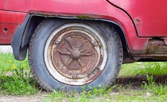 Weathered car wheel with dirt and grime. Rusty abandoned car in the parking lot. Restoration of a retro car. Flat tire. Vintage wheel with classic red car cap. photo