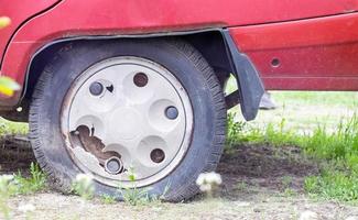 Weathered car wheel with dirt and grime. Rusty abandoned car in the parking lot. Restoration of a retro car. Flat tire. Vintage wheel with classic red car cap. photo