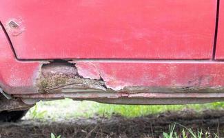 Rusty driver's door sills. Corrosion of the body of a red old car after winter. Influence of reagents in winter on an unprotected vehicle body. Damage to the left side, rotten threshold on the bottom. photo