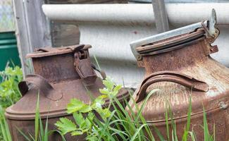 Two old rusty metal cans in the countryside. Container for transporting liquids, milk or liquid fuels with several handles. Milk bank of a cylindrical form with a wide mouth. Flask with sealed lid. photo