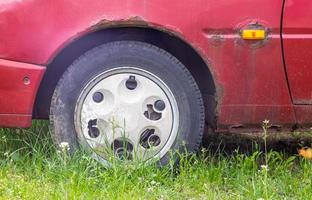 Weathered car wheel with dirt and grime. Rusty abandoned car in the parking lot. Restoration of a retro car. Flat tire. Vintage wheel with classic red car cap. photo