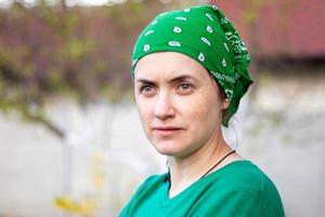 Portrait, close-up. Beautiful young woman without makeup in green t-shirt and green sun hat on a sunny summer day outdoors. Sunbeam. Caucasian woman gardener or farmer wears a modern headscarf. photo