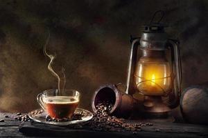 Coffee cup glass and vintage kerosene lamp oil lantern burning with glow soft light aged wood floor photo