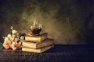 Coffee in cup glass on old books and rose on aged wood floor photo
