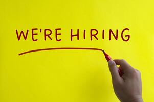 Hand writing we are hiring on yellow cover background. photo