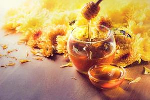 Honey in glass jar with bee flying and flowers on a wooden floor photo