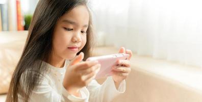 asian little girl playing with smartphone, technology and communication concept - smiling girl texting on smartphone and lying in bed at home photo