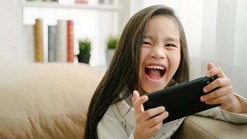 asian little girl playing with smartphone, technology and communication concept - smiling girl texting on smartphone and lying in bed at home photo