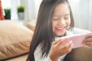 asian little girl playing with smartphone, technology and communication concept - smiling girl texting on smartphone and lying in bed at home photo
