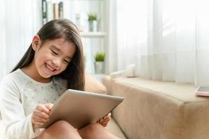 Cute child using a smartphone and smiling while sitting on sofa at home photo