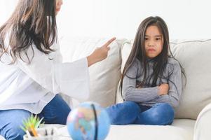 Angry asian mother sitting with little daughter , mom scolds for discipline bad behaviour capricious kid, family generations problems, misunderstanding concept photo