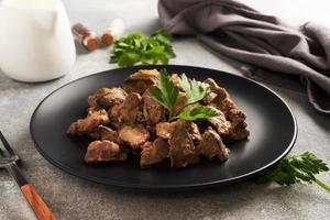 Fried or baked chicken liver with onion and sauce, green parsley leaves on a plate. Meat dish enriched with iron.