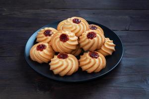 Kurabye shortbread cookies with berry jam in a black plate. Delicious dessert, dark wooden background with copy space. photo
