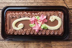 Chocolate rectangular cake decorated with cream roses. Sweet food is a confectionery business. Top view photo