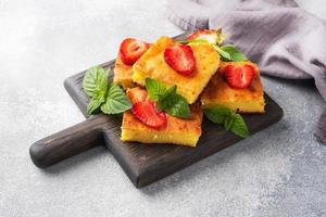 Cottage cheese casserole with strawberries and mint. Delicious homemade dessert made of curd and fresh berries with cream. Gray concrete background, copy space. photo