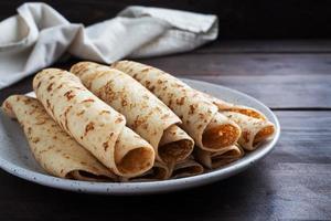 Thin pancakes rolled into a roll on a plate. The concept of a delicious breakfast or Maslenitsa. wooden background.