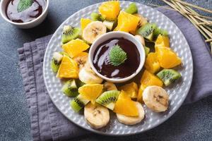 Chocolate fondue with fruit on a dark concrete background. concept summer party. Copy space photo