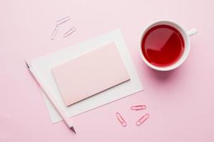 Red-pink objects. Cup of tea and Notepad for text on pastel pink background. Copy space. Top view Flat lay photo