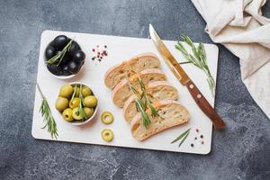 Italian ciabatta bread with olives and rosemary on a cutting Board. Dark concrete background. Copy space. photo