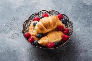 Croissants with fresh raspberries and blueberries on a dark concrete background. Copy space. concept of Breakfast coffee honey. photo