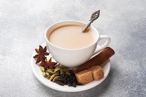 bebida india té masala con leche y especias. palitos de cardamomo canela anís estrellado azúcar de caña. espacio de copia de mesa gris concreto. foto