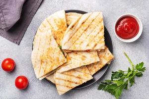 Triangular slices of a Mexican quesadilla with the sauce. The traditional dish of Mexico is tortillas stuffed with meat and vegetables. photo