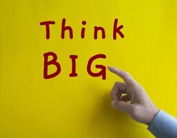 Hand pointing Think Big text on yellow cover background. photo