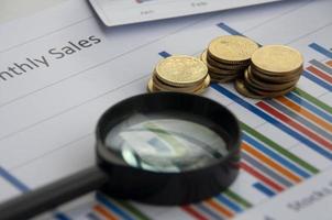 Analysis of data, chart and graphs with magnifying glass and gold coins background. Business finances concept photo