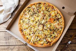 Freshly baked pizza in a cardboard box on a wooden table. photo