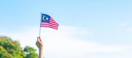 mano que sostiene la bandera de malasia sobre fondo de cielo azul. septiembre día nacional de malasia y agosto día de la independencia foto