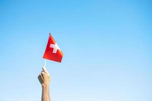 mano que sostiene la bandera suiza sobre fondo de cielo azul. día nacional de suiza y conceptos de celebración feliz foto