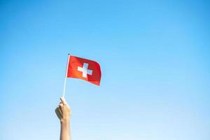 mano que sostiene la bandera suiza sobre fondo de cielo azul. día nacional de suiza y conceptos de celebración feliz foto