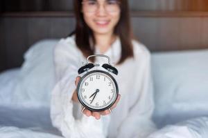 Woman holding alarm clock on bed, happy female wake up in the morning. daily routine, sleep, relaxing and have a nice day concepts photo