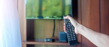 mano usando el control remoto para ajustar la televisión inteligente dentro de la habitación moderna en casa o en un hotel de lujo foto