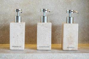 Toiletries bottles in bathroom at luxury hotel or modern home. shower container set, body shower gel, shampoo and hair conditioner in ceramic ware with wall background photo