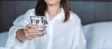 Happy woman holding water glass, female drinking pure water on bed at home. Healthy, Refreshment, lifestyle concept photo