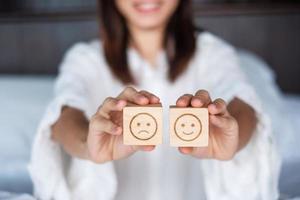 Woman holding smile and angry emotion face block. Customer choose Emoticon for user reviews. Service rating, mental health, positive thinking, satisfaction, evaluation and feedback concept photo